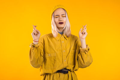 Portrait of young woman gesturing against yellow background