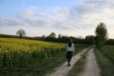 Rear view of woman walking on field against sky