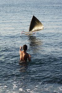 Rear view of shirtless man against boat in sea