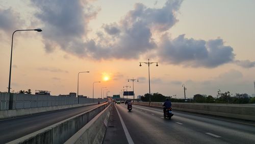 Vehicles on road against sky during sunset