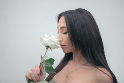 Side view of young woman holding flower against wall