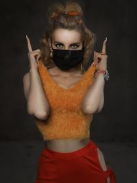 Portrait of beautiful young woman wearing mask against black background