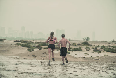 Rear view of men running on beach against clear sky