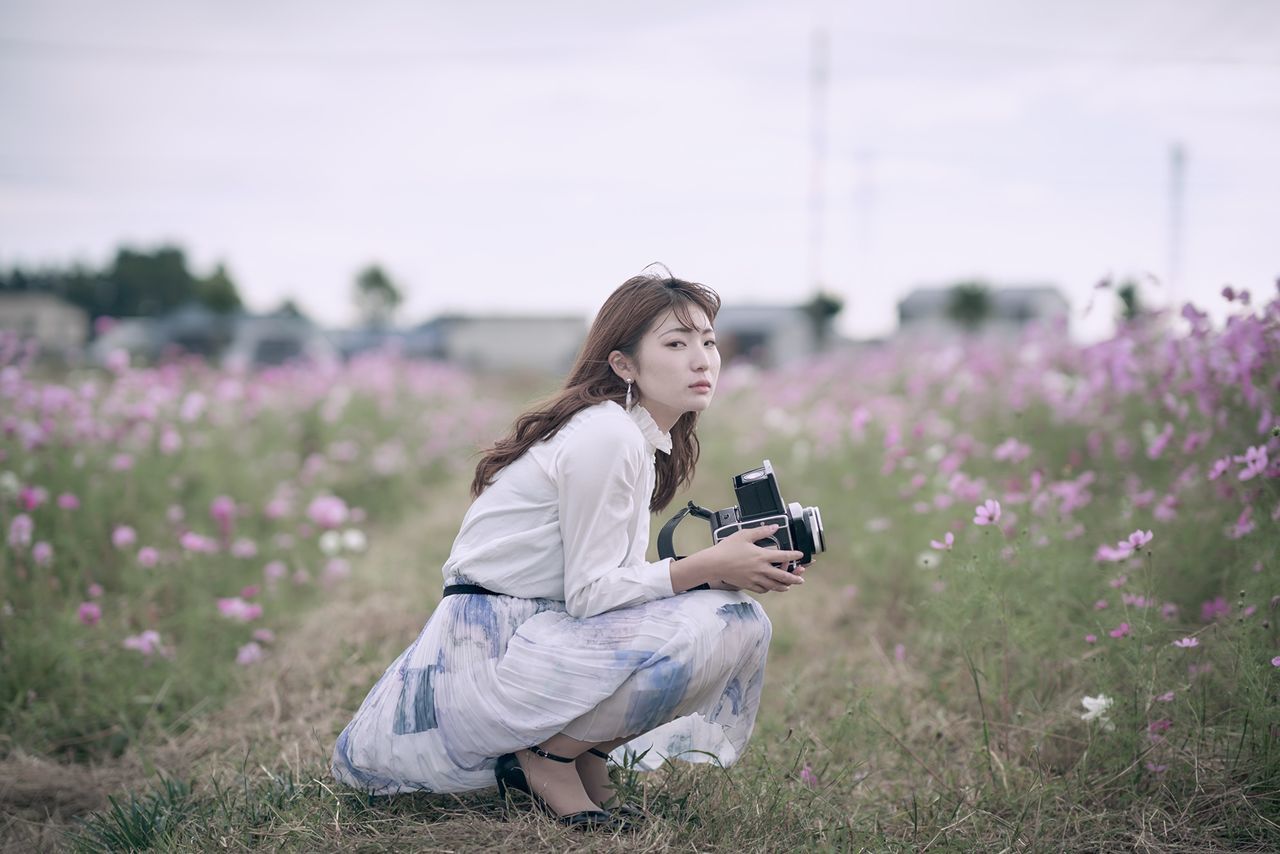 one person, land, field, leisure activity, flower, young adult, plant, lifestyles, young women, flowering plant, nature, real people, technology, photography themes, camera - photographic equipment, growth, beauty in nature, full length, outdoors, hairstyle, beautiful woman