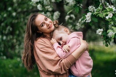 Young mother with her daughter in her arms in a blooming apple orchard