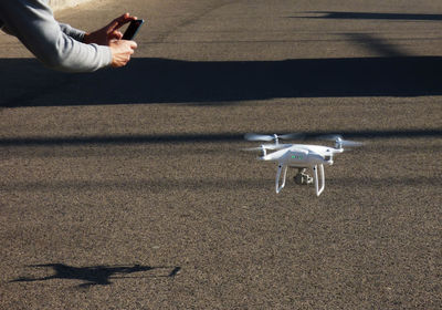 Cropped hands of man photographing drone flying over street