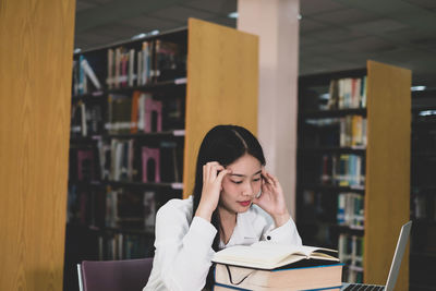 Young woman reading book while sitting in library