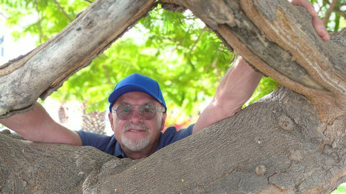 Portrait of smiling senior man by tree trunk