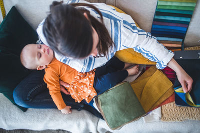 High angle view of design professional working while sitting with sleeping daughter on sofa at home office