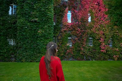 Rear view of woman standing on field against ivy covered building