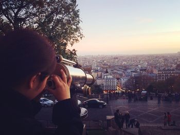 Woman looking at cityscape through coin-operated binoculars during sunset