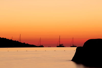 Silhouette sailboats in sea against orange sky