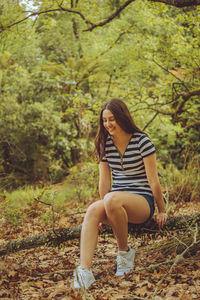 Full length of woman sitting on tree in forest