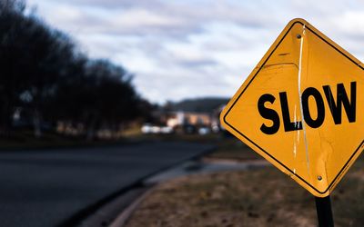 Close-up of road sign by road against cloudy sky