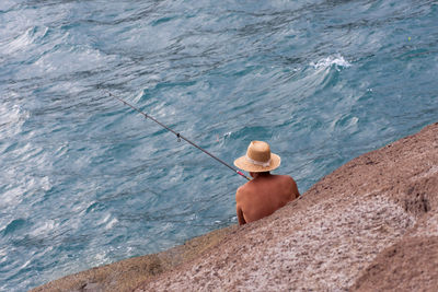 Rear view of man fishing at seaside 