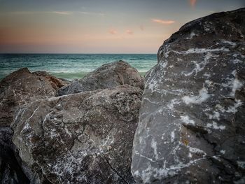 Rocks at seashore against sky during sunset