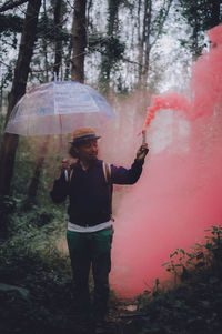 Man with umbrella and red smoke standing in forest