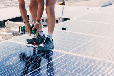 Anonymous male engineer using electric screwdriver and installing contemporary solar battery at factory