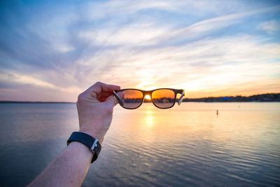 Close-up of hand against sea during sunset