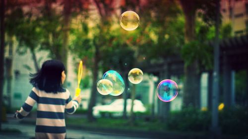 Rear view of girl blowing bubbles at park