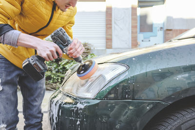 A young caucasian guy  is drilling a drill with a disk with a sponge and polishing the headlight