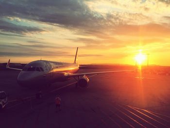 Airplane on airport runway against sky during sunset