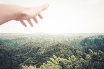 Cropped hand gesturing towards green mountains