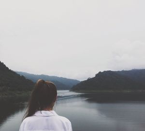 Rear view of woman standing by lake against sky