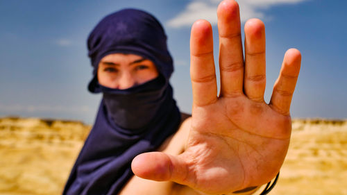 Portrait of man showing stop gesture while standing against sky