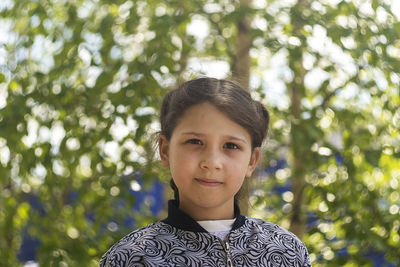 Girl 8 year old against green tree. day, horizontal shot front view.