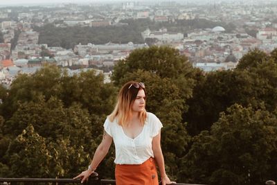 Beautiful young woman standing against trees in city