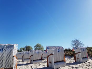 Hooded chairs on beach against clear blue sky