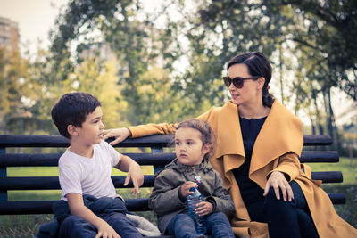 Family sitting on bench against trees at park