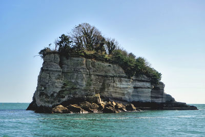 Rock formation by sea against clear sky