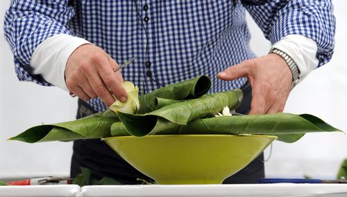 Midsection of man putting leaves and flowers in bowl