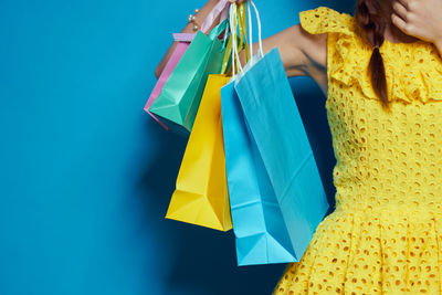 Midsection of woman holding shopping bags against blue background