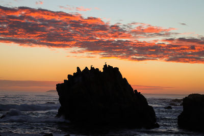 Silhouette of rock at seaside during sunset