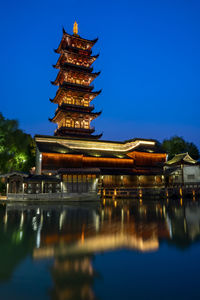 Reflection of temple in lake by building against clear sky