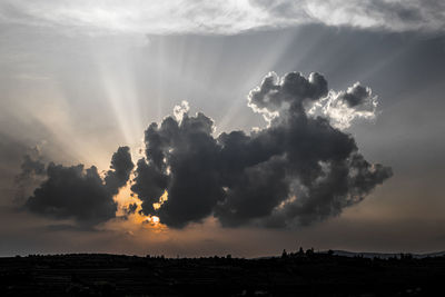 Sunlight streaming through clouds over silhouette landscape