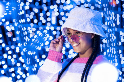 Joyful woman of color with a white beanie braided hairstyle and pink glasses enjoying the christmas