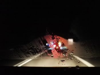 Close-up of raindrops on illuminated car