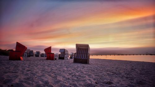 Hooded chairs on sand at beach against sky during sunset