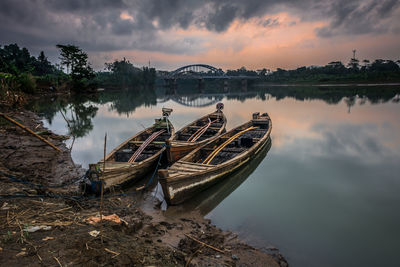 Boat moored at shore against sky during sunset