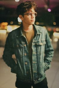 Young man looking away while standing on street in city at night