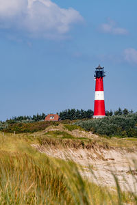 Lighthouse on field by building against sky