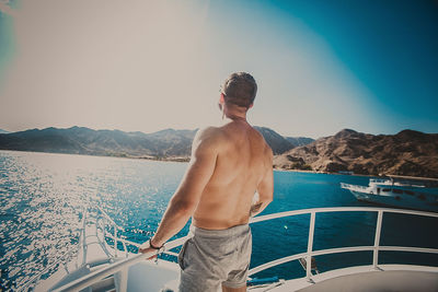 Shirtless man standing on boat in sea against sky