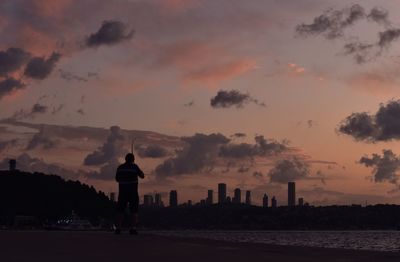 Rear view of silhouette man standing by cityscape against sky during sunset