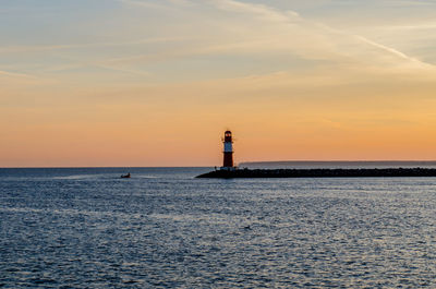 Lighthouse by sea against sky during sunset