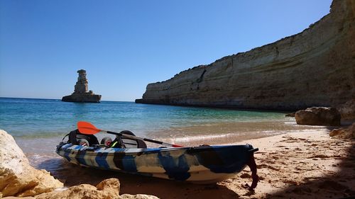 Boats on rocks by sea against clear blue sky