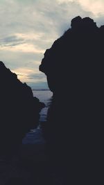 Silhouette man on cliff by sea against sky during sunset